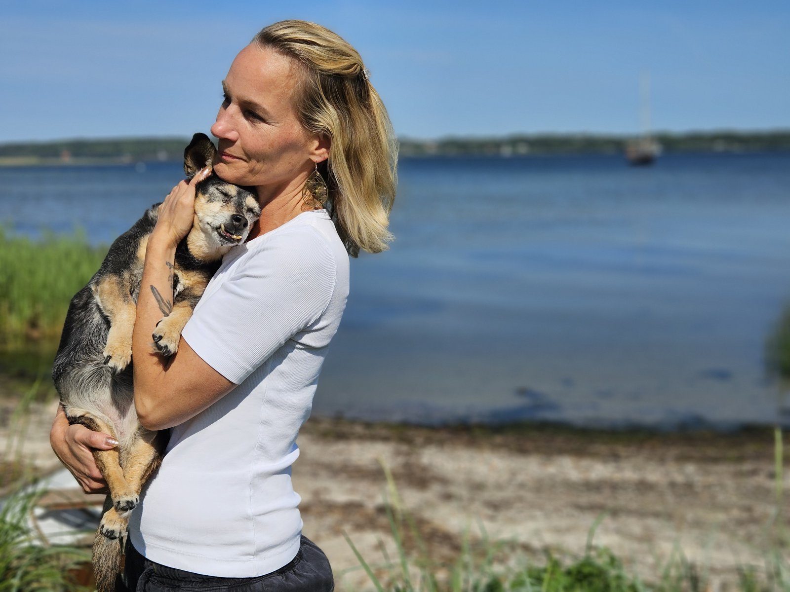 Tierkommunikatorin Melinda Weber hält ihren Hund im Arm, im Hintergrund das Wasser